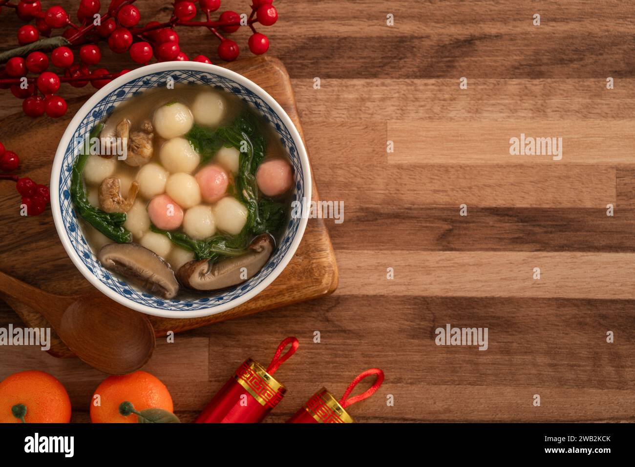 Eating red and white small tangyuan, tang yuan, glutinous rice dumpling balls with savory soup in a bowl on wooden table background for lunar new year Stock Photo