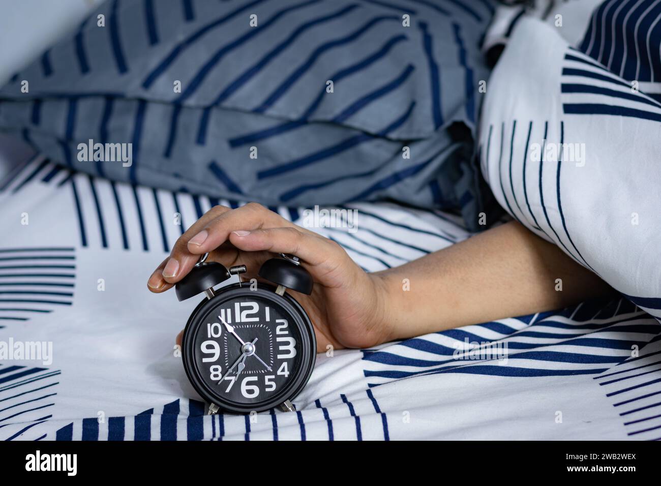 Man's hand holding an alarm clock in bed. time to wake up Stock Photo