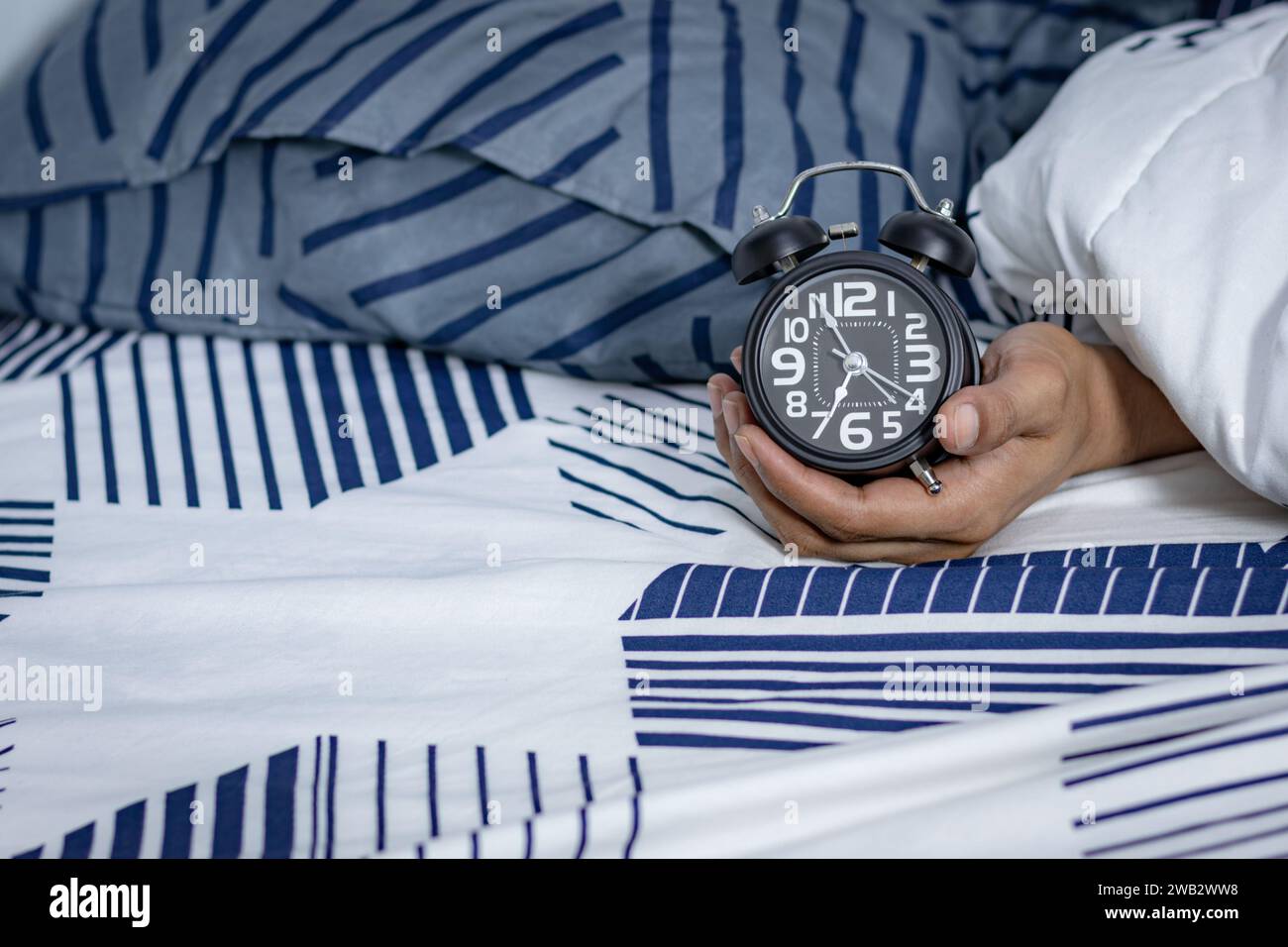 Man's hand holding an alarm clock in bed. time to wake up Stock Photo