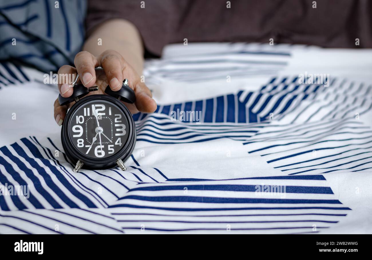 Man's hand holding an alarm clock in bed. time to wake up Stock Photo