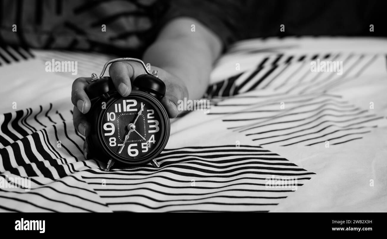 Man's hand holding an alarm clock in bed. time to wake up Stock Photo