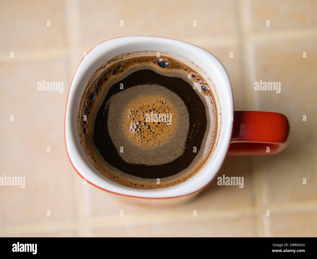 Red cup (white inside) of freshly brewed coffee on a ceramic tile countertop Stock Photo