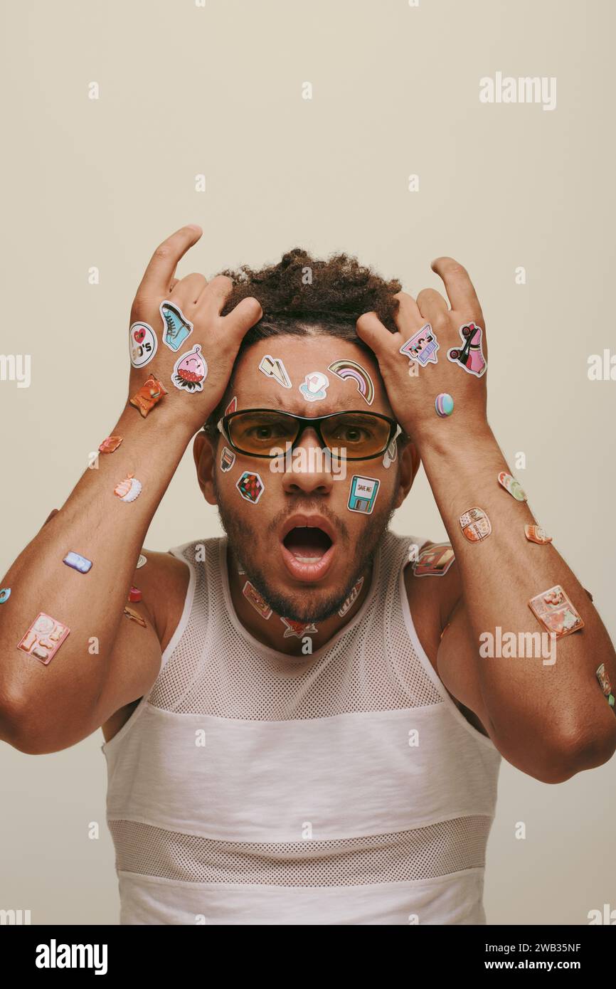 shocked young african american man in sunglasses with trendy stickers on face on grey background Stock Photo