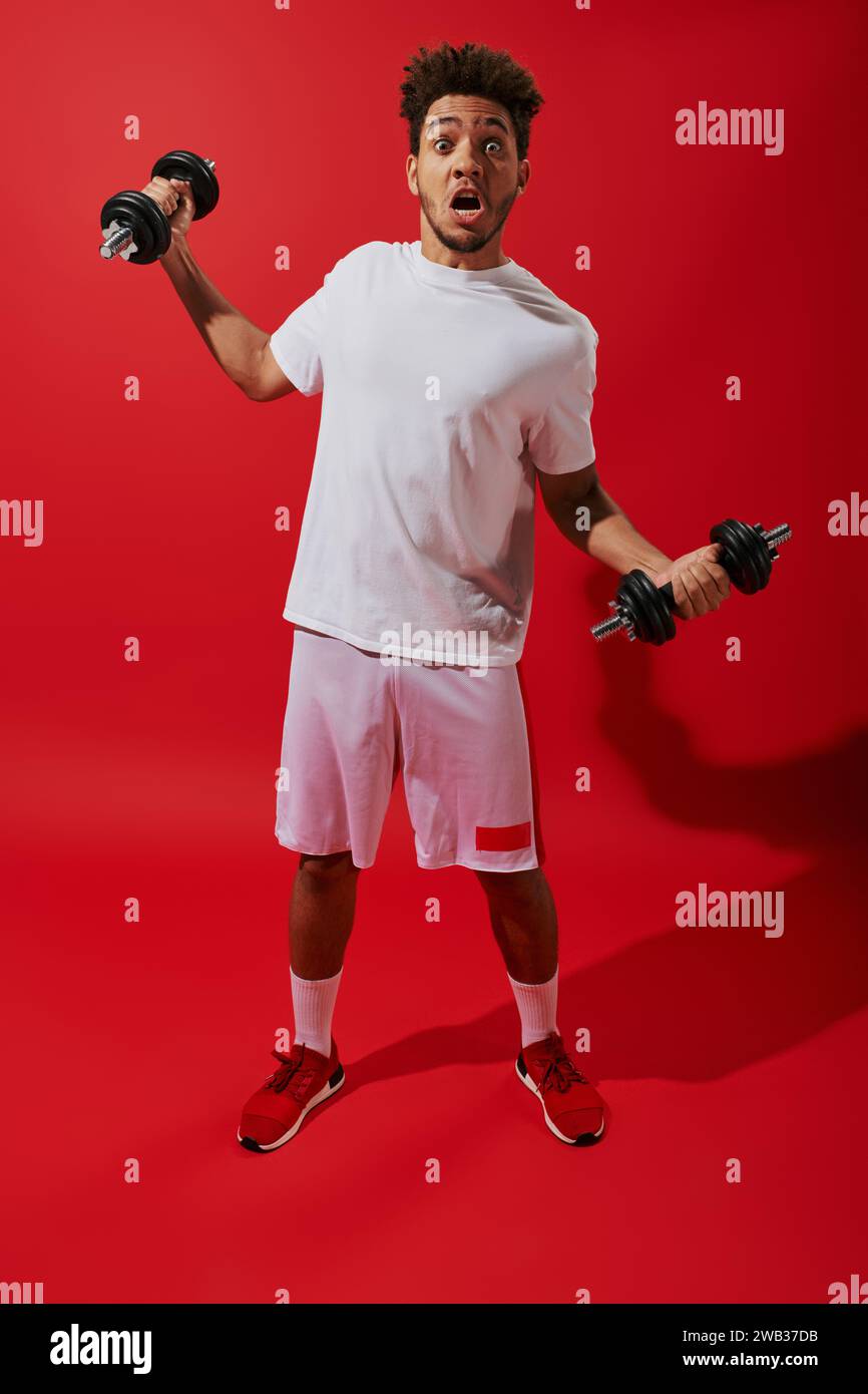 shocked african american sportsman working out with heavy dumbbells on ...