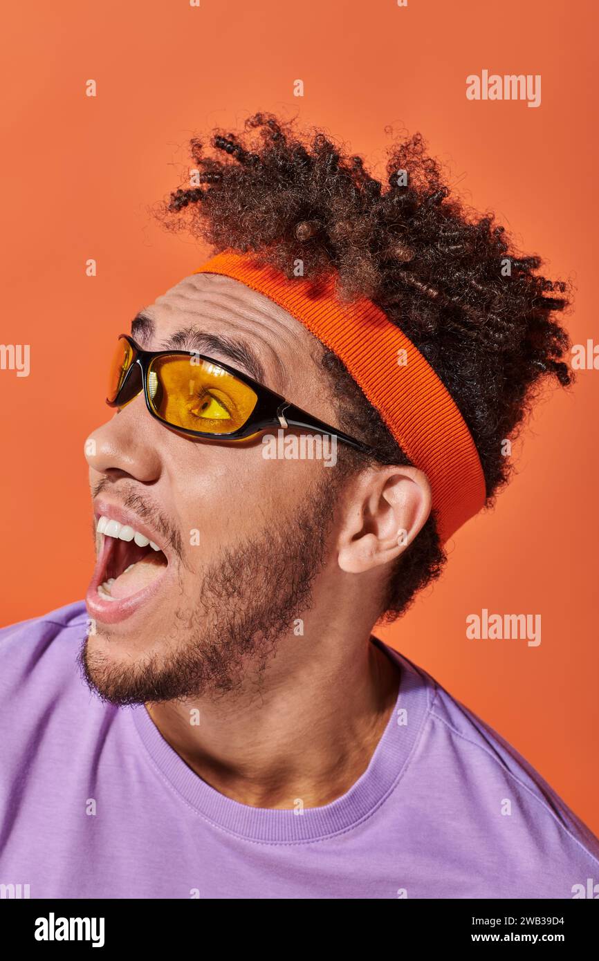 excited african american man in eyeglasses and headband on orange