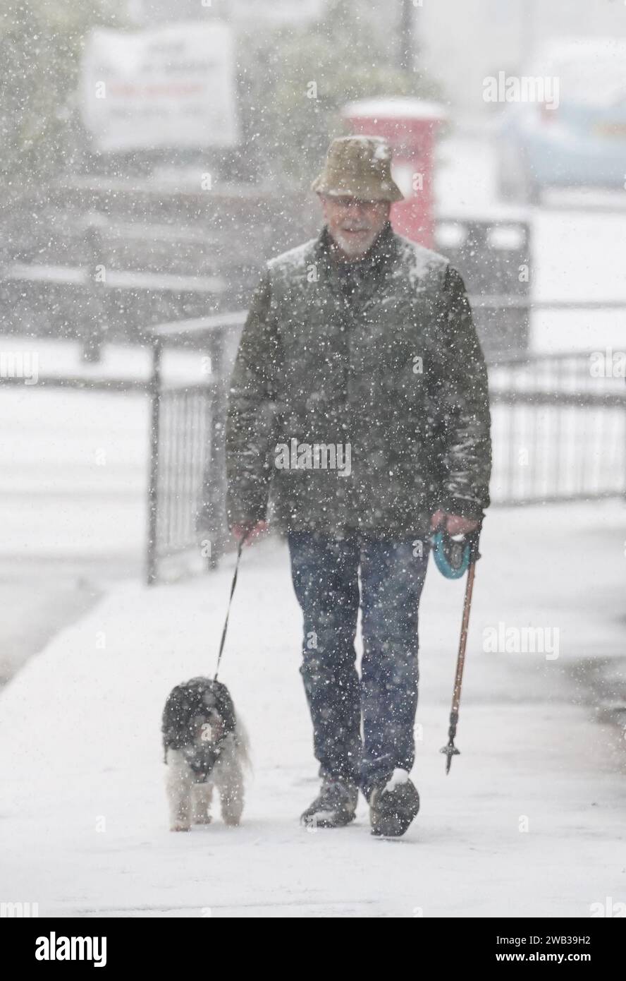 A man walks dog through a snow flurry in Lenham, Kent. Sleet and snow showers have been forecast for parts of the country on Monday as some regions are still trying to grapple with flooding following intense rainfall. Picture date: Monday January 8, 2024. Stock Photo