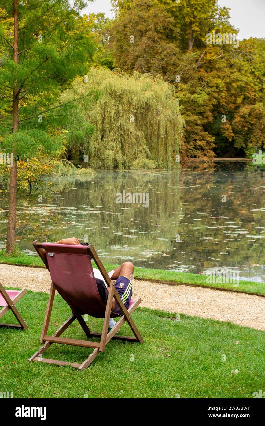 UK, England, Oxfordshire, Oxford, Worcester College, Garden, student reading in deckchair beside lake Stock Photo