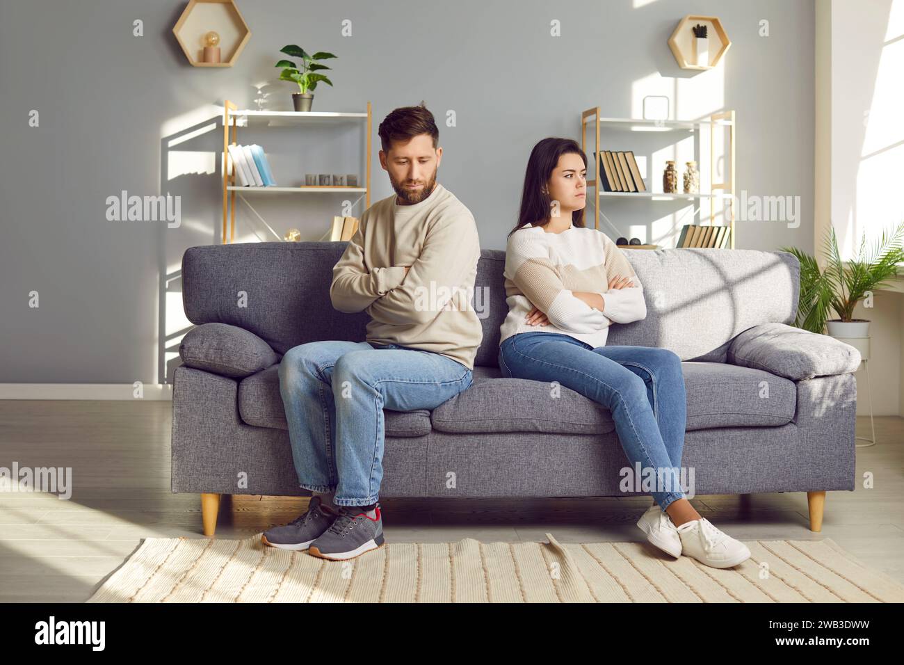 Angry young husband and wife are sitting back to back on the couch after a quarrel Stock Photo
