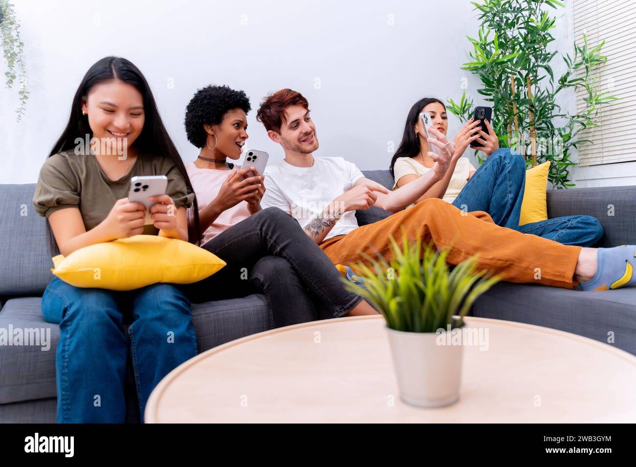 Diverse friends smiling and using smartphones on a sofa, enjoying tech interaction. Stock Photo