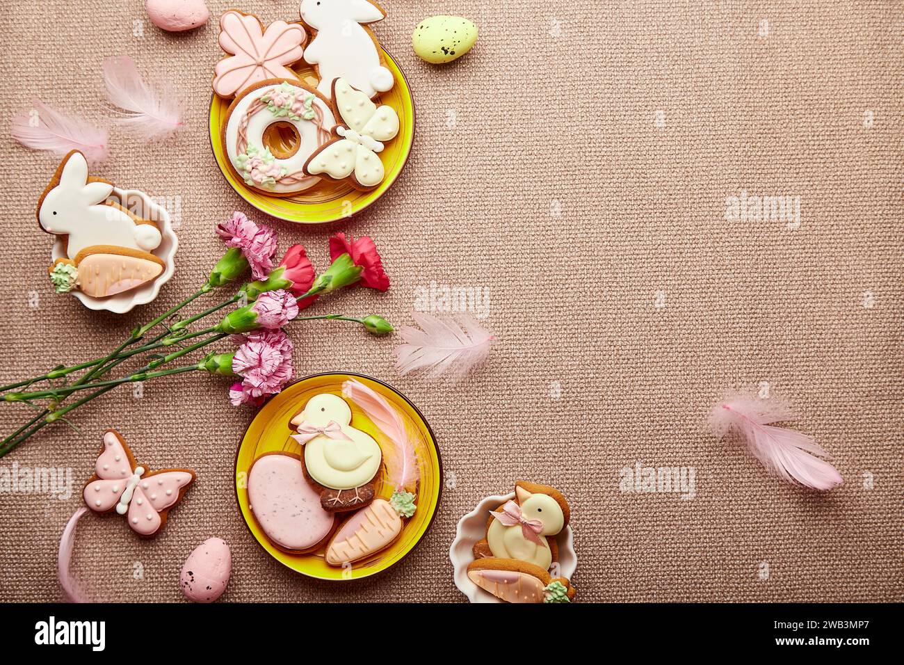 Aesthetic Easter flat lay with copy space. Decorated Easter cookies, pink flowers with feathers. Spring background. Stock Photo