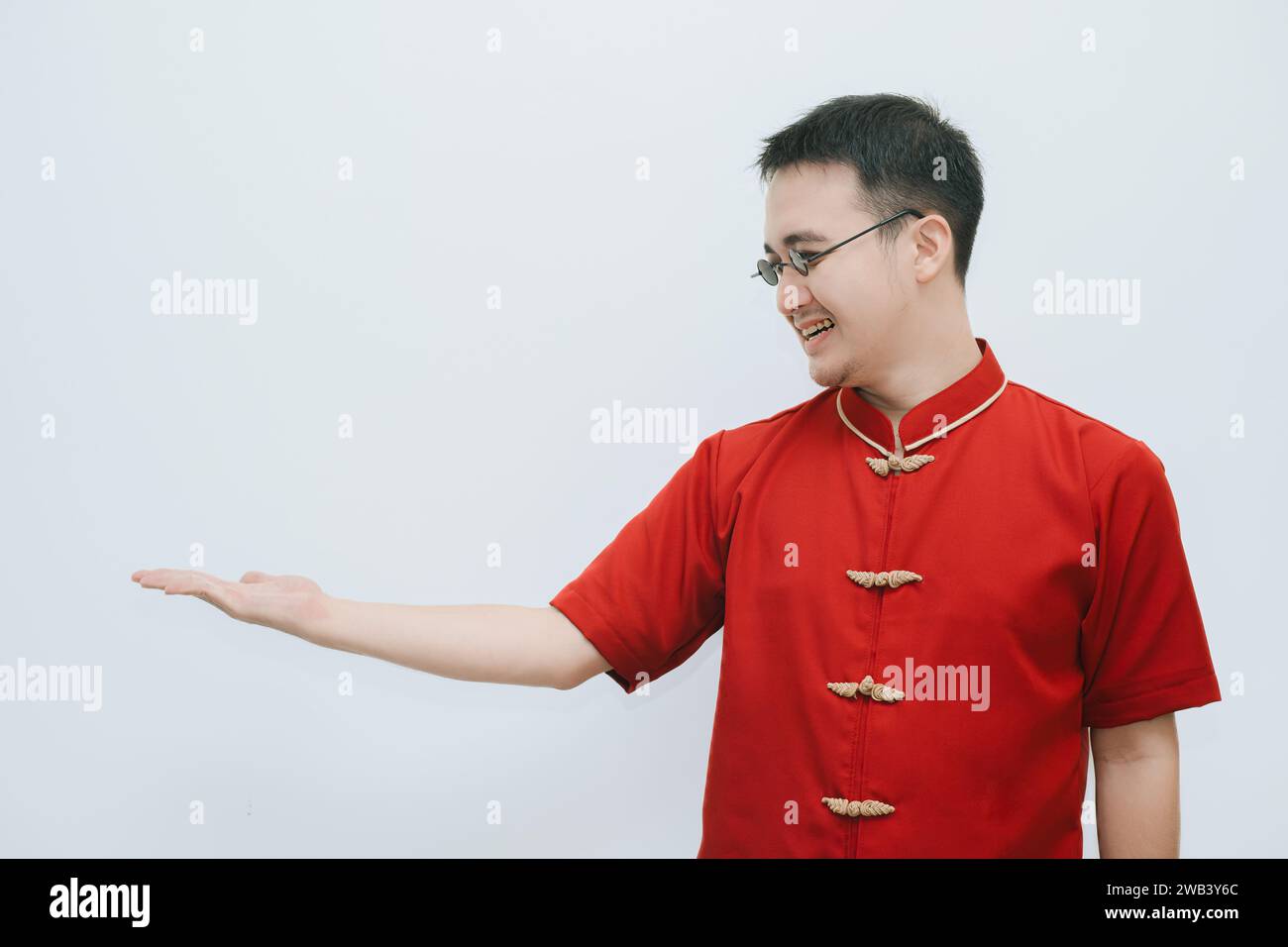 Happy face of Asian man wearing Cheongsam and black vintage sunglasses is opens his arm to the left side and looking at it on white background Stock Photo