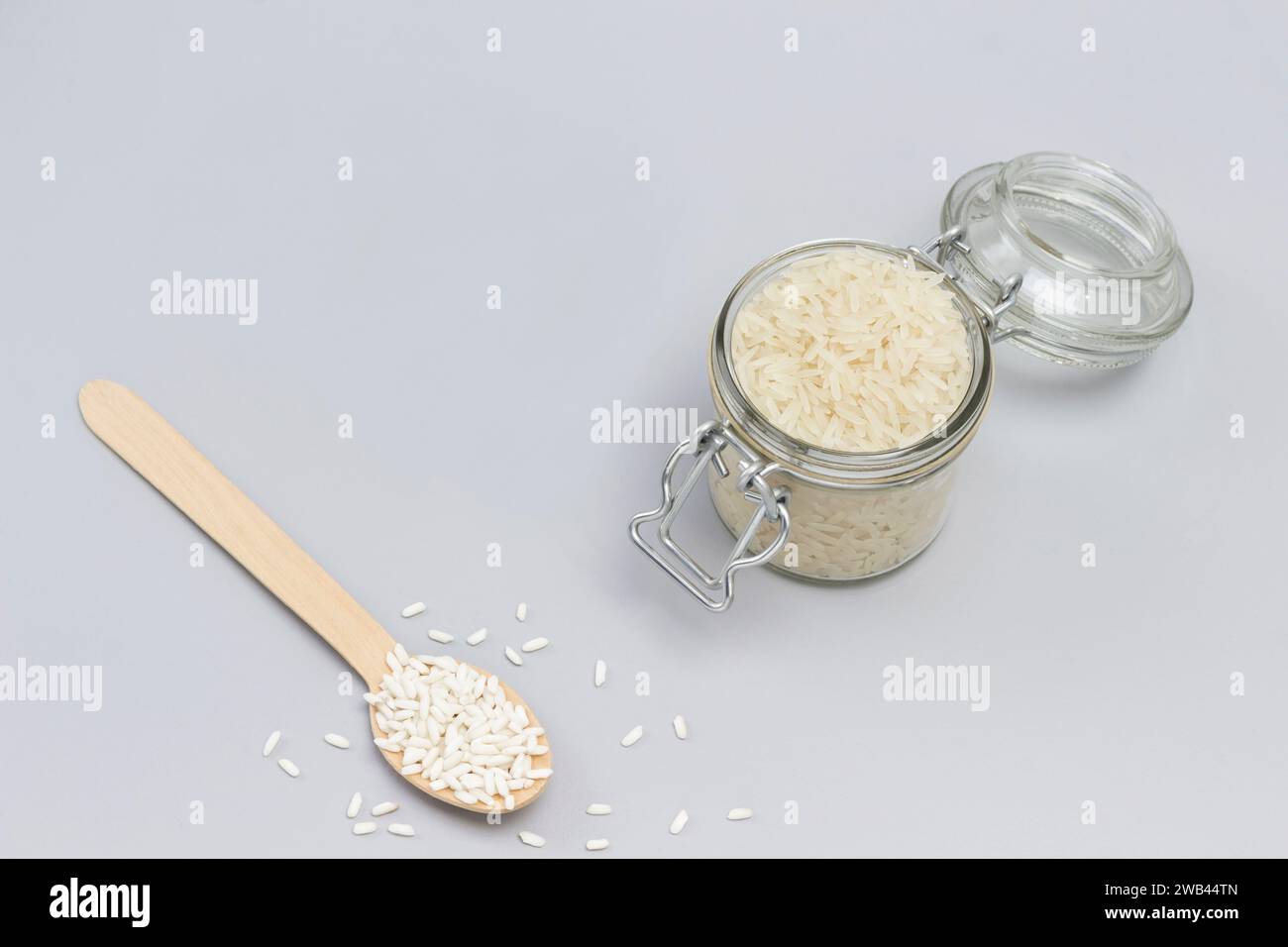 Three types of white rice in glass jar, wooden spoon and bowl. Top view. Gray background Stock Photo