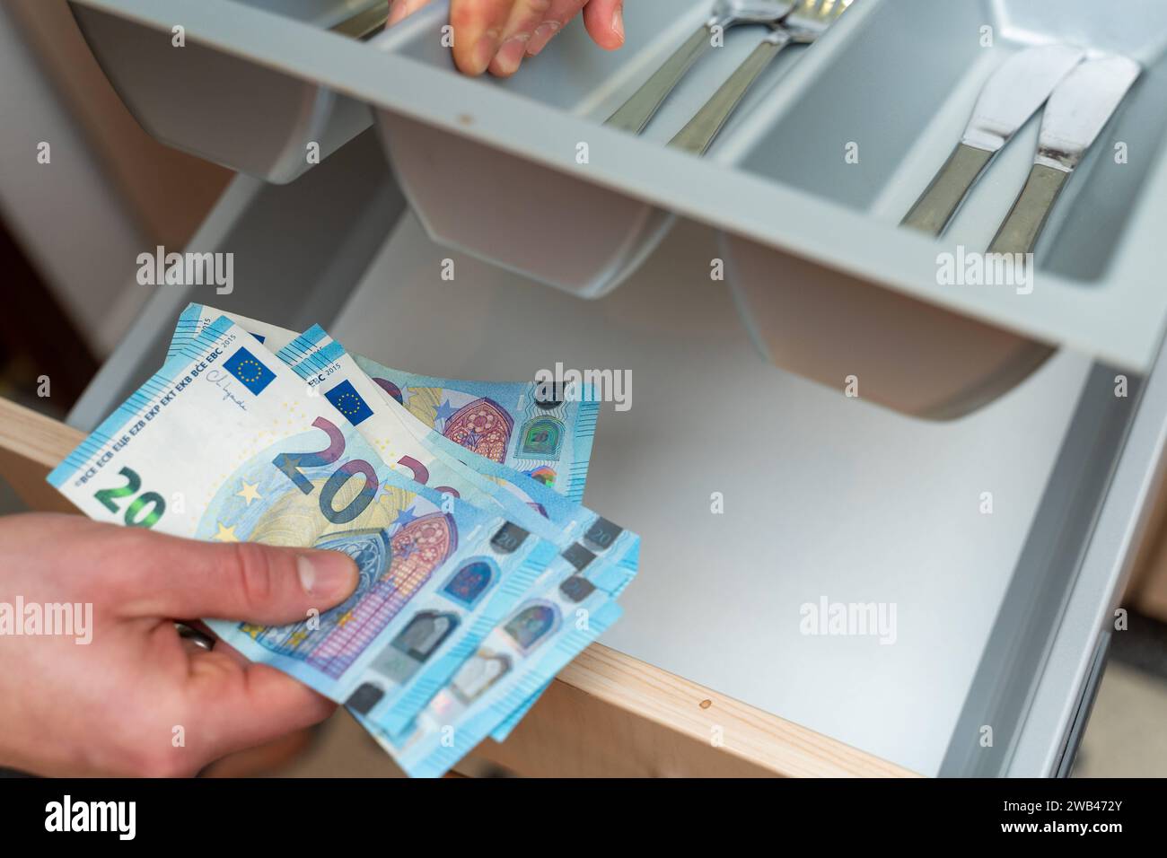 Bavaria, Germany - January 6, 2024: Man hides euro banknotes in a drawer in the kitchen. Money hiding concept *** Mann versteckt Euro Geldscheine in einer Schublade in der Küche. Geldversteck Konzept Stock Photo