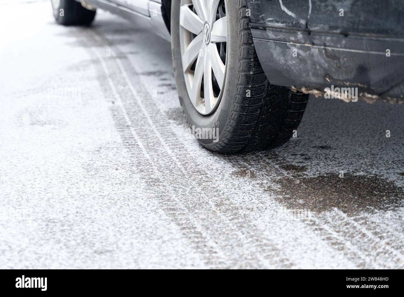 Bavaria, Germany - 8 January 2024: Snow and ice on a road with a tire track behind a tire from a car *** Schnee und Eis auf einer Straße mit Reifenspur hinter einem Reifen von einem Auto Stock Photo
