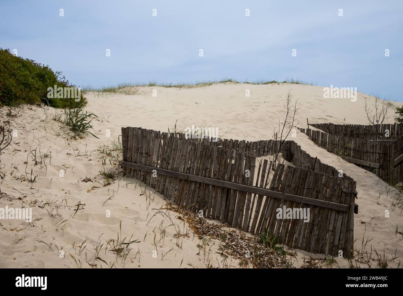 Sand dune made of white sand. on the seaside. Broken wooden fence. Grass, plants and bushes. Cloudy sky in the spring. Spiaggia (beach) Portu Tramatzu Stock Photo