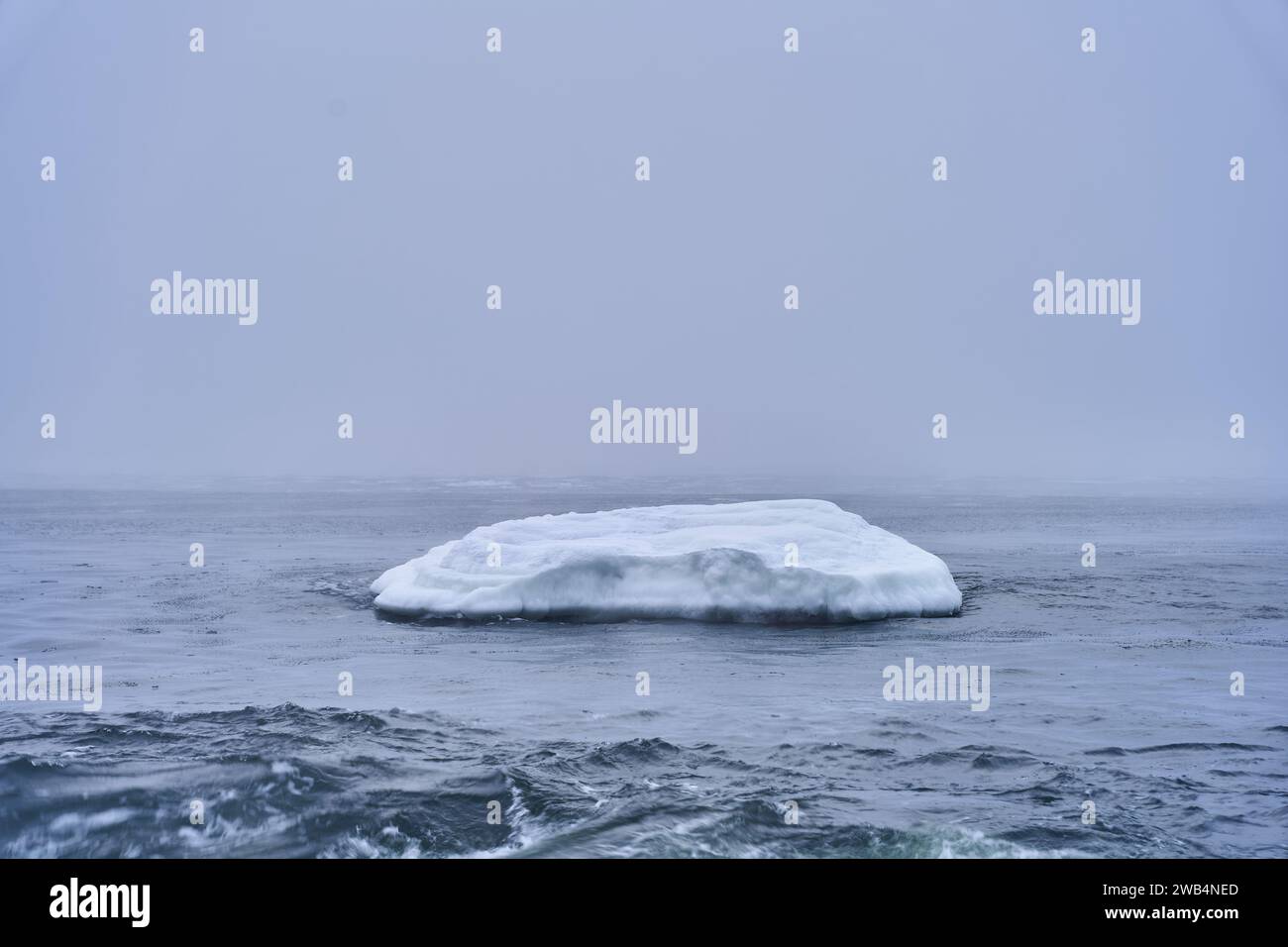 A majestic iceberg floats peacefully in a tranquil ocean shrouded in a mysterious fog Stock Photo