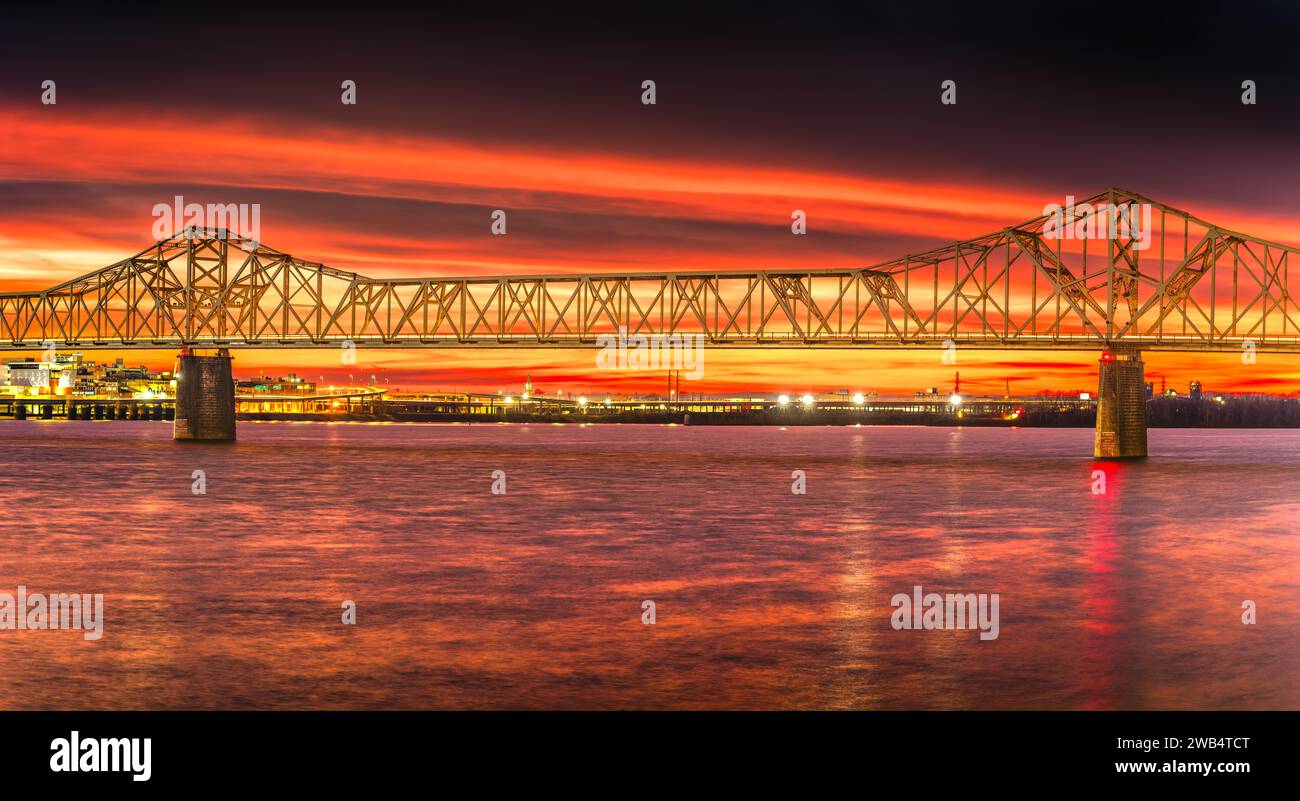 A scenic view of a bridge spanning across a body of water, with a vibrant red sky illuminated in the background Stock Photo