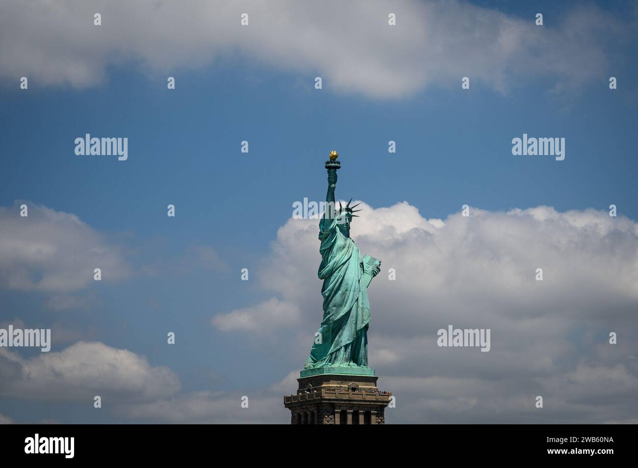 New York's Statue of Liberty in the center of the image with blue sky and clouds. Stock Photo