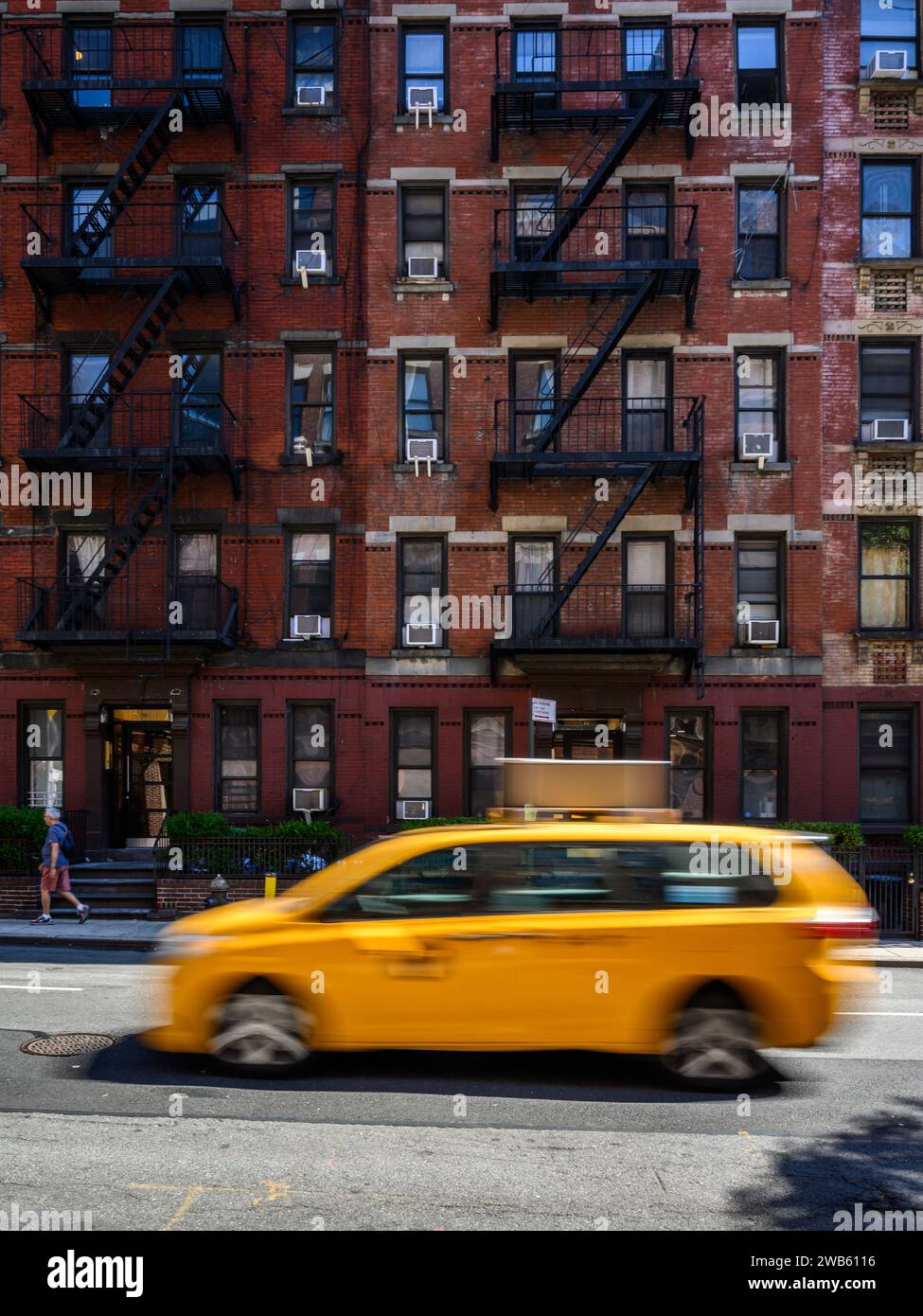 Typical old New York building with metal fire escape stairs with a yellow cab moving down the street. Stock Photo