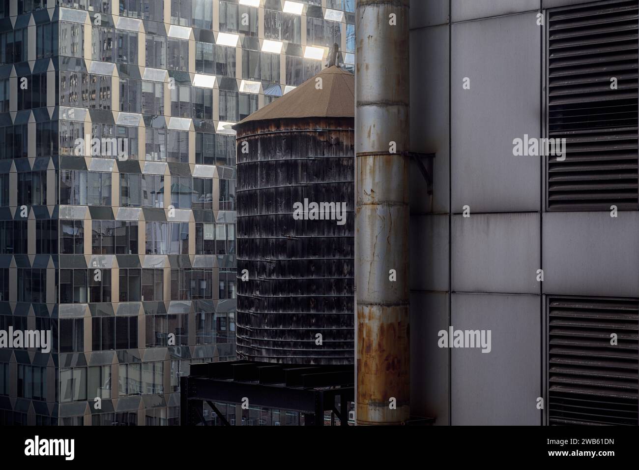 Detail of a modern glass building against an old building with a water tank in downtown New York, USA. Stock Photo