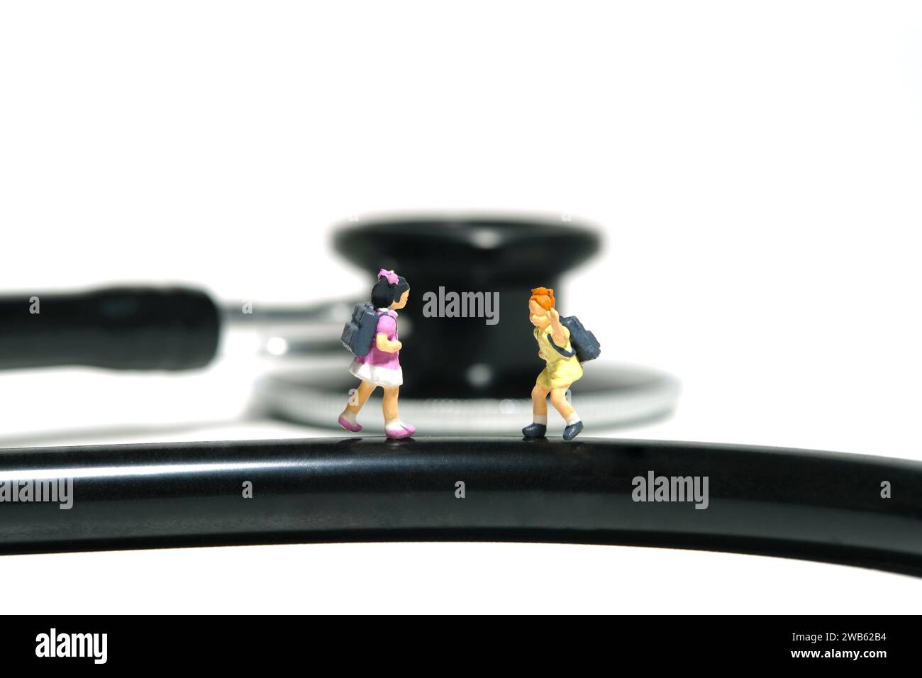 Miniature people toy figure photography. Two girl students standing above stethoscope, saying goodbye, sick leave. Isolated on white background. Image Stock Photo