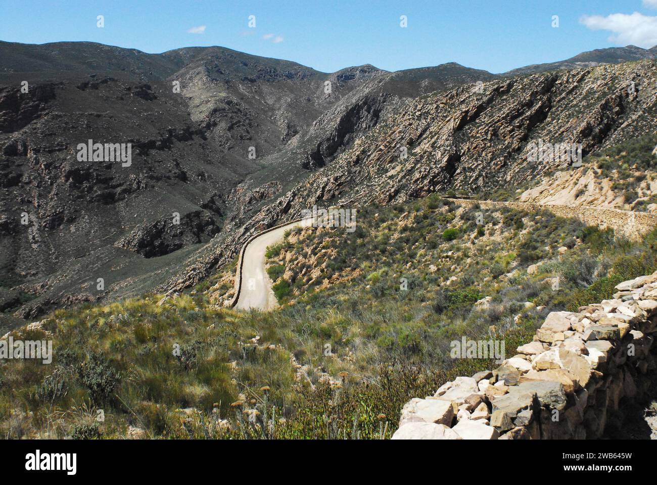 Panoramic overview of a rough, narrow, winding dirt road through the remote Swartberg mountains near Knysna, South Africa on a sunny Summer day. Stock Photo