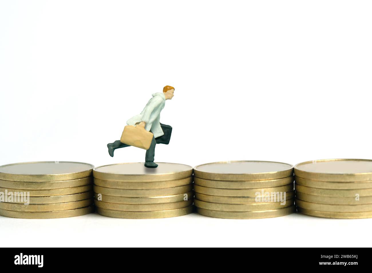 Miniature tiny people toy figure photography. A businessman wearing coat running above flat coin stack. Isolated on white background. Image photo Stock Photo