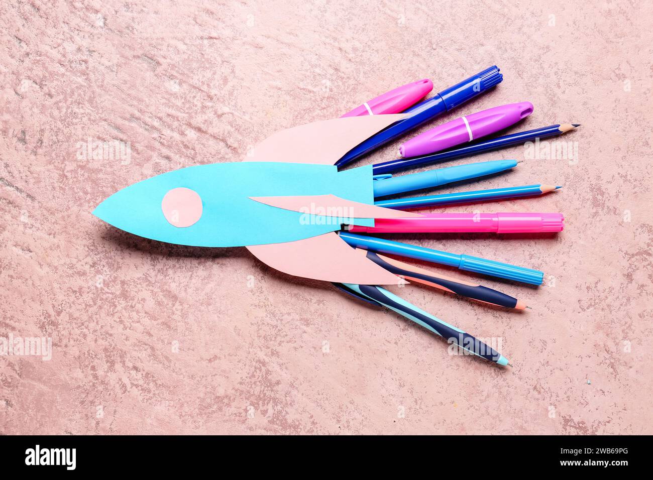 Blue paper rocket with pens, pencils and markers on pink grunge ...