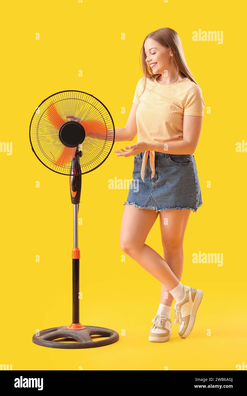 Young woman with electric fan on yellow background Stock Photo - Alamy