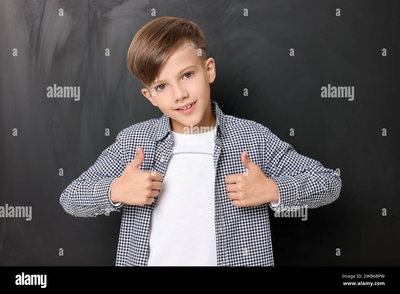 Cute schoolboy showing thumbs up near chalkboard Stock Photo - Alamy