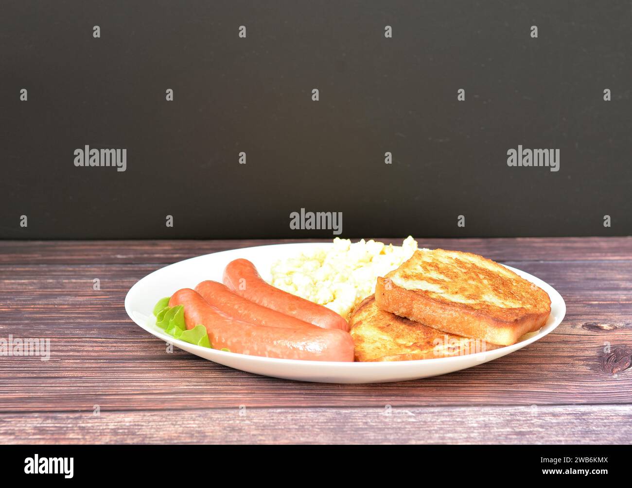 Egg omelette, boiled sausages and bread croutons with lettuce on a wooden table. Close-up. Stock Photo