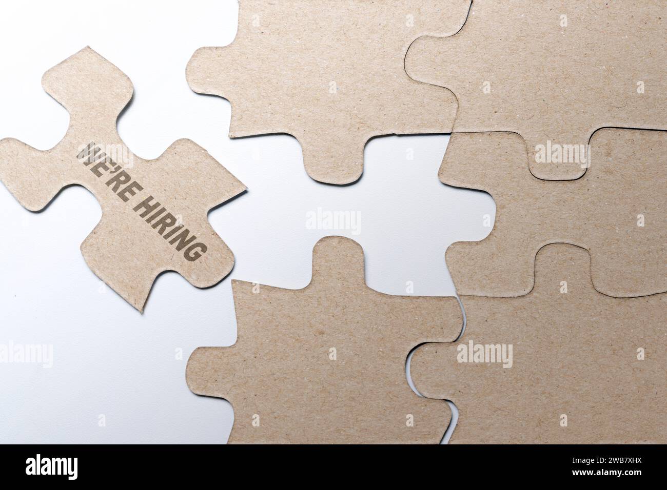Piece of missing jigsaw puzzle with We're Hiring text over white background. Human resources