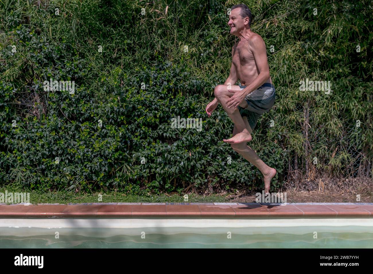 Middle-aged white man dives into the pool by jumping from the side edge with a funny expression Stock Photo