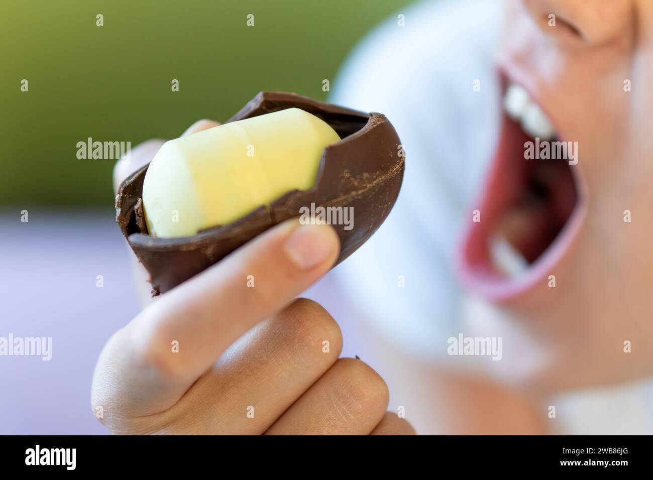 A baby girl bites a chocolate egg with a plastic toy inside. harmful
