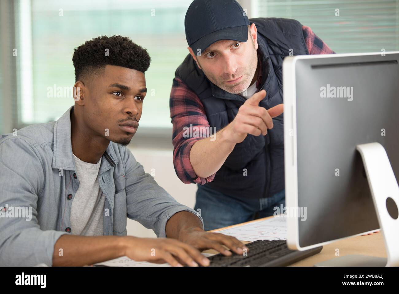 two men conferring while looking at computer screen Stock Photo