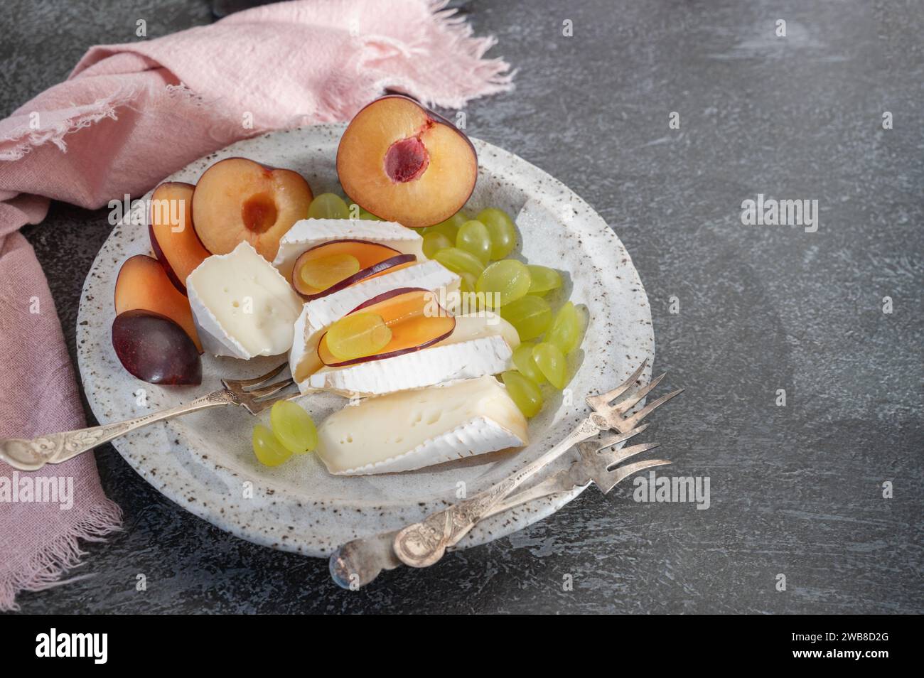 Camembert brie cheese with grapes and plums. Camembert and brie, sliced into bite-size pieces. Cheese served on handmade plates. Top view, flat displa Stock Photo