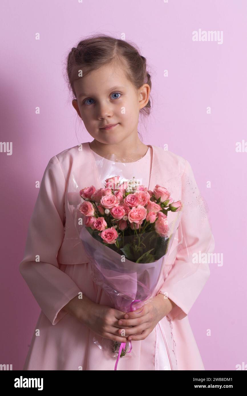 A cute little girl in a pink dress holds a bouquet of pink roses on a ...