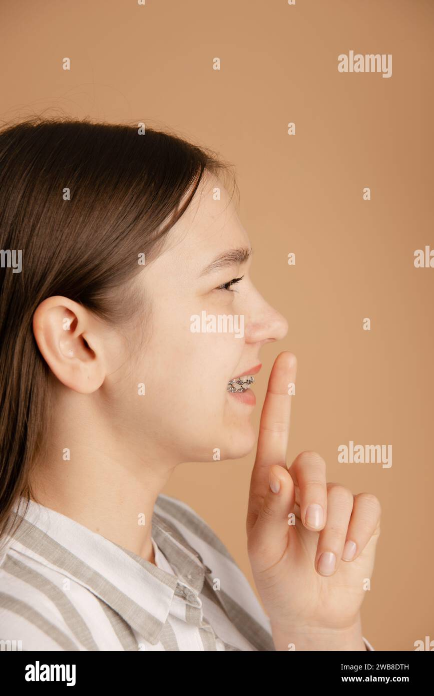 young side face woman with braces show shhh gesture on beige background. no conversations and keep quiet Stock Photo