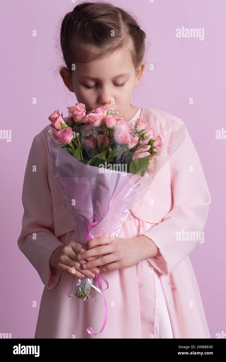A cute little girl in a pink dress holds a bouquet of pink roses on a ...