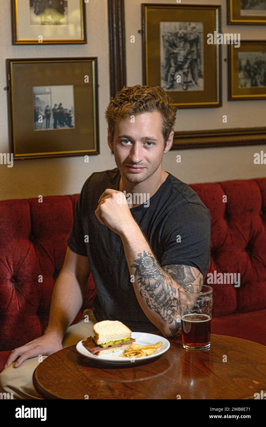 Young man eating cheese toastie and drinking a pint of ale in traditional London pub . Stock Photo