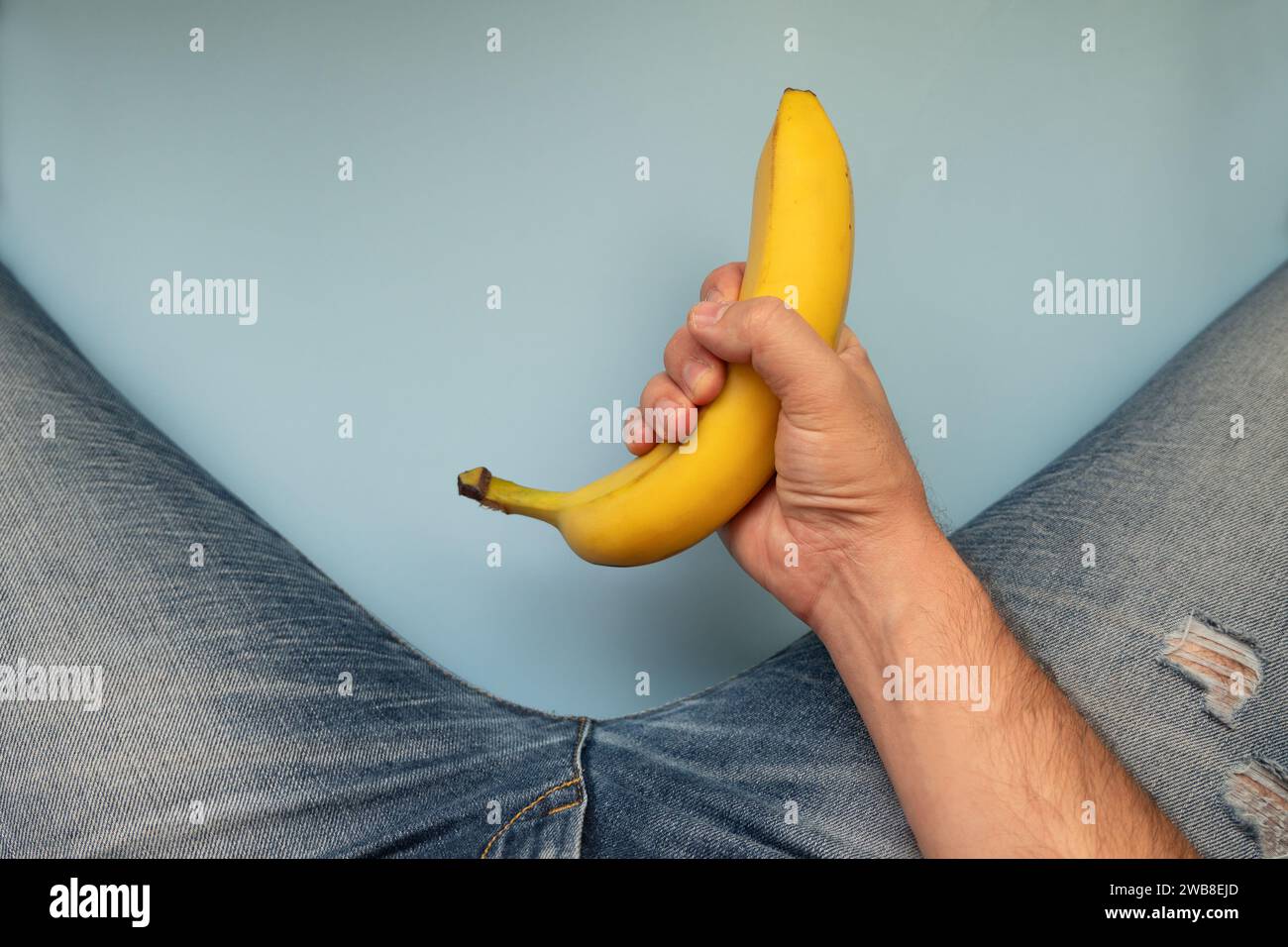 A yellow big banana and men's legs in jeans on a blue background. The concept of men's health Stock Photo