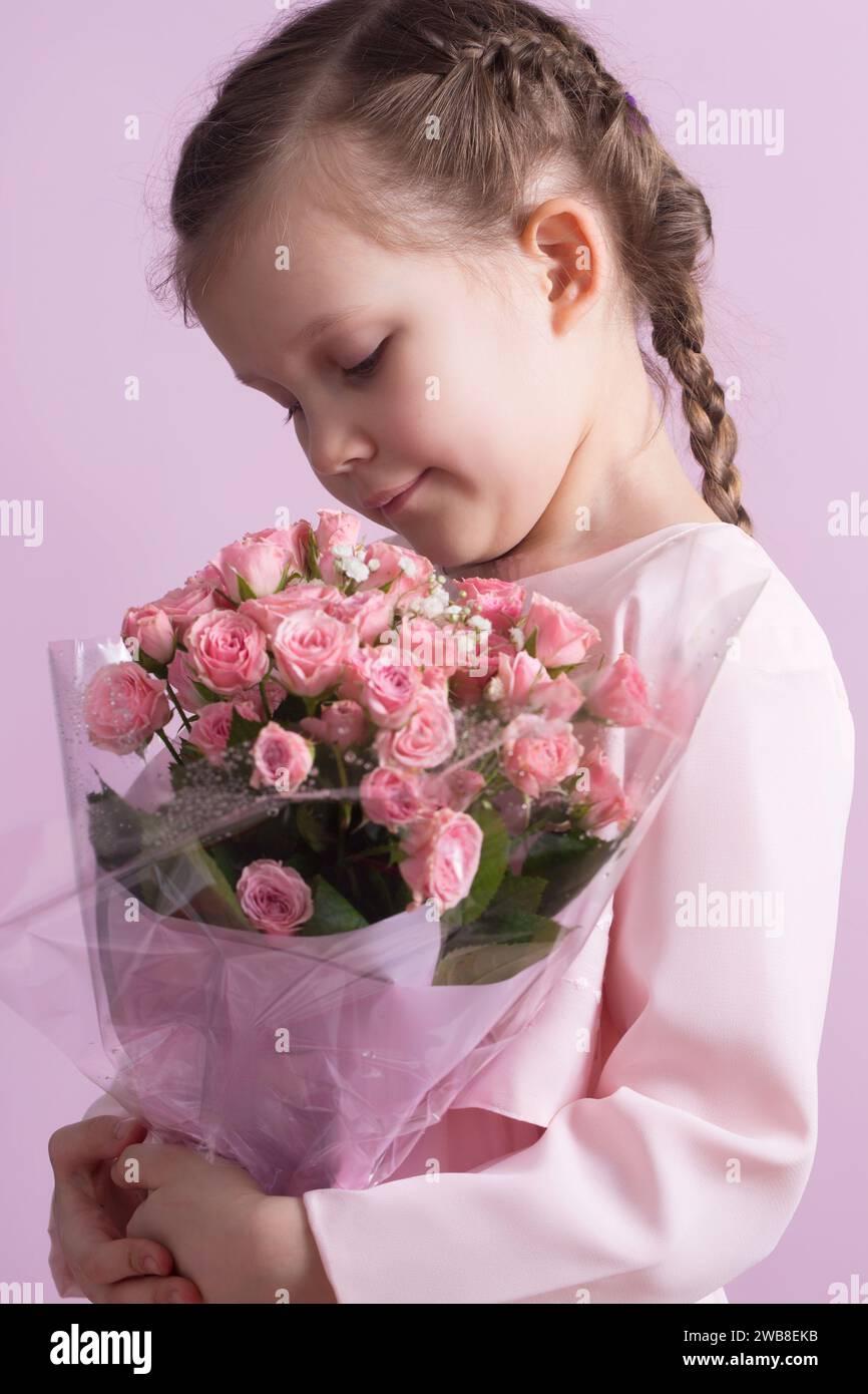 A cute little girl in a pink dress holds a bouquet of pink roses on a ...