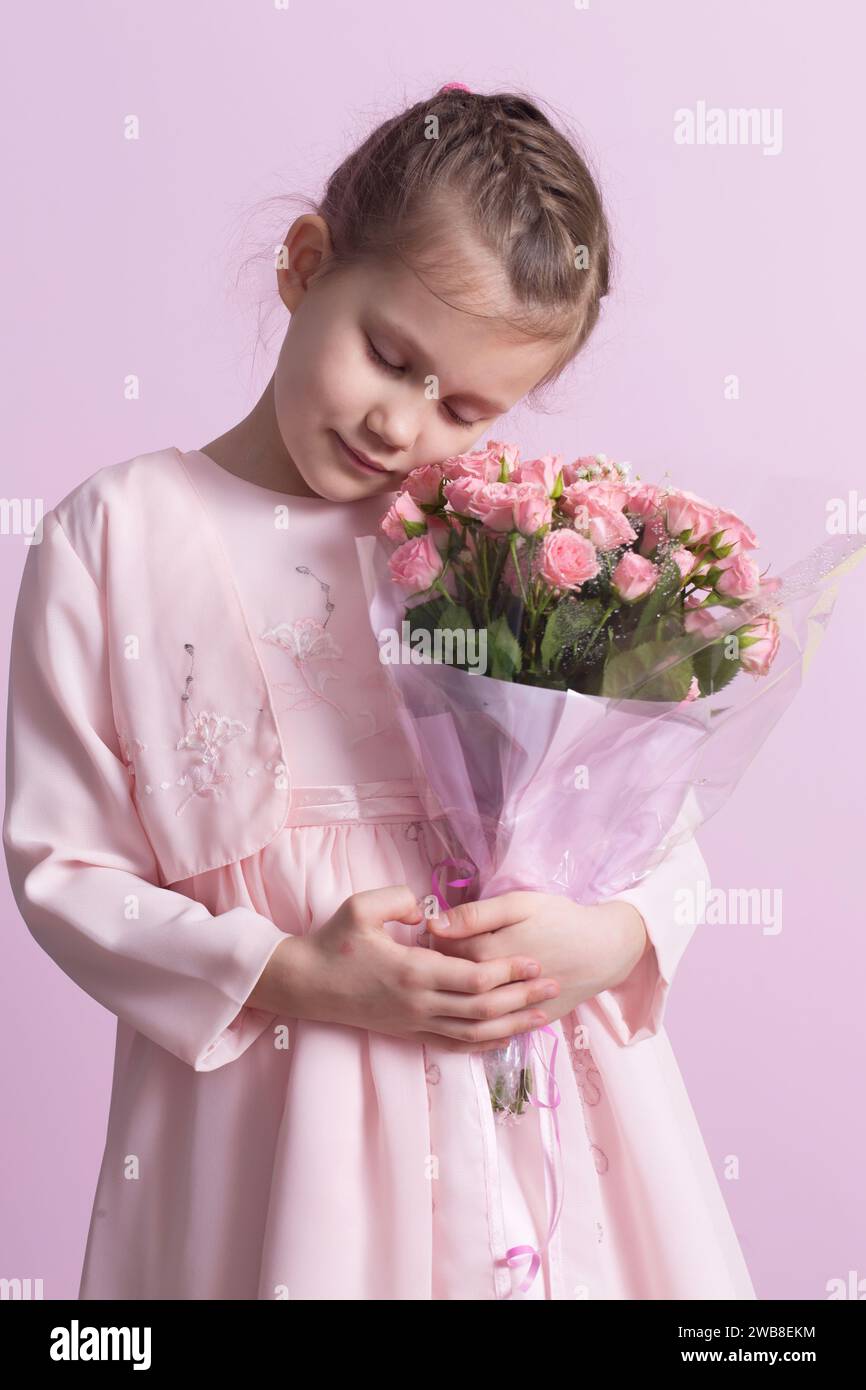 A cute little girl in a pink dress holds a bouquet of pink roses on a ...