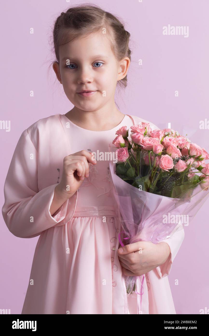 A cute little girl in a pink dress holds a bouquet of pink roses on a ...