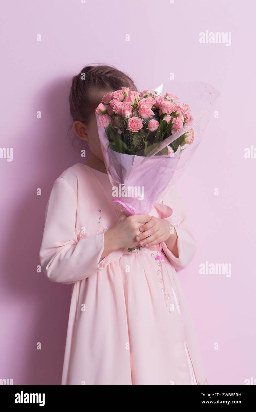 A cute little girl in a pink dress holds a bouquet of pink roses on a ...