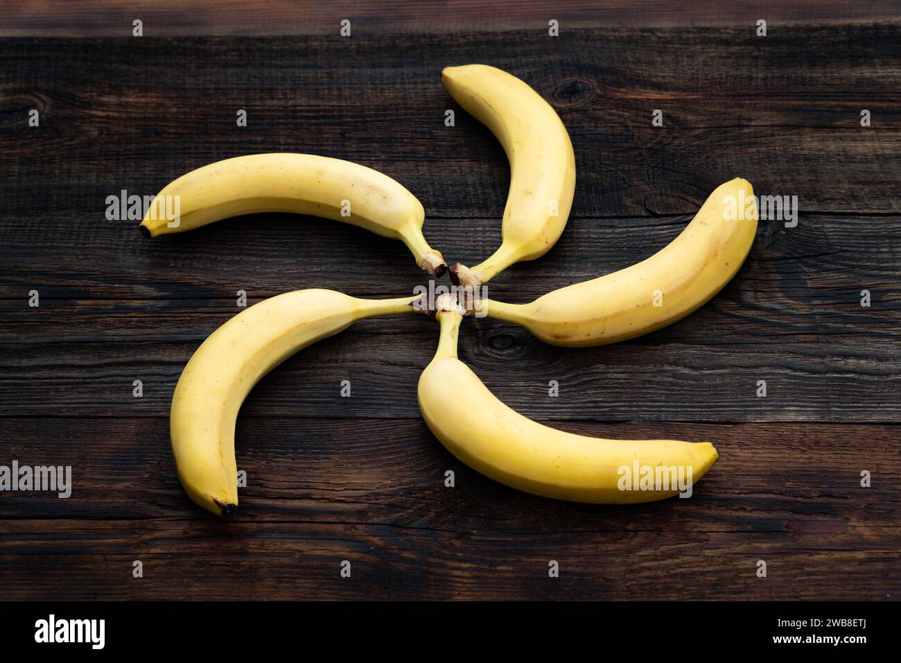 Bananas on a wooden table. a ripe yellow bunch of bananas on the kitchen table. view from above. bananas are stacked in the shape of the sun, circle Stock Photo
