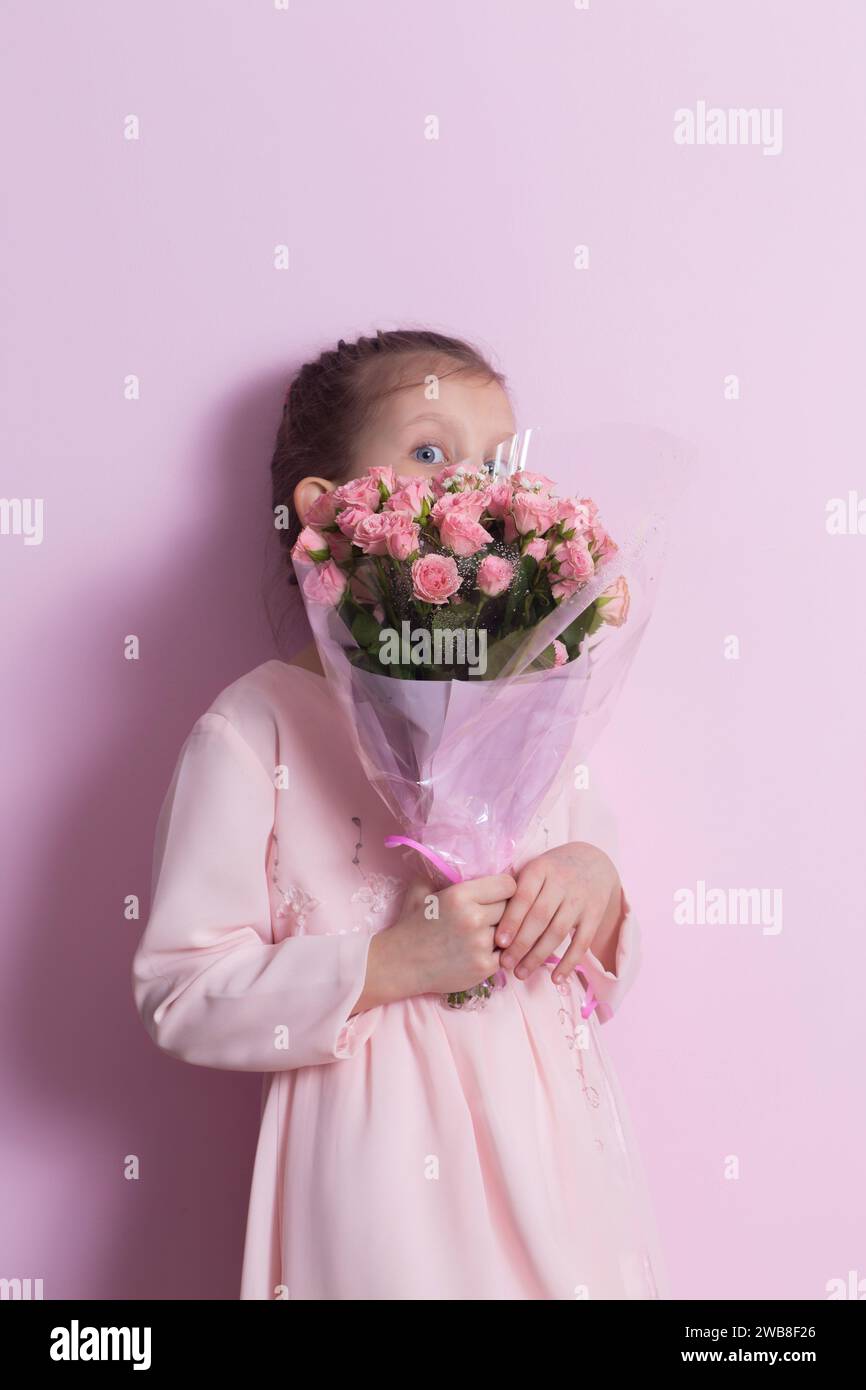 A cute little girl in a pink dress holds a bouquet of pink roses on a ...