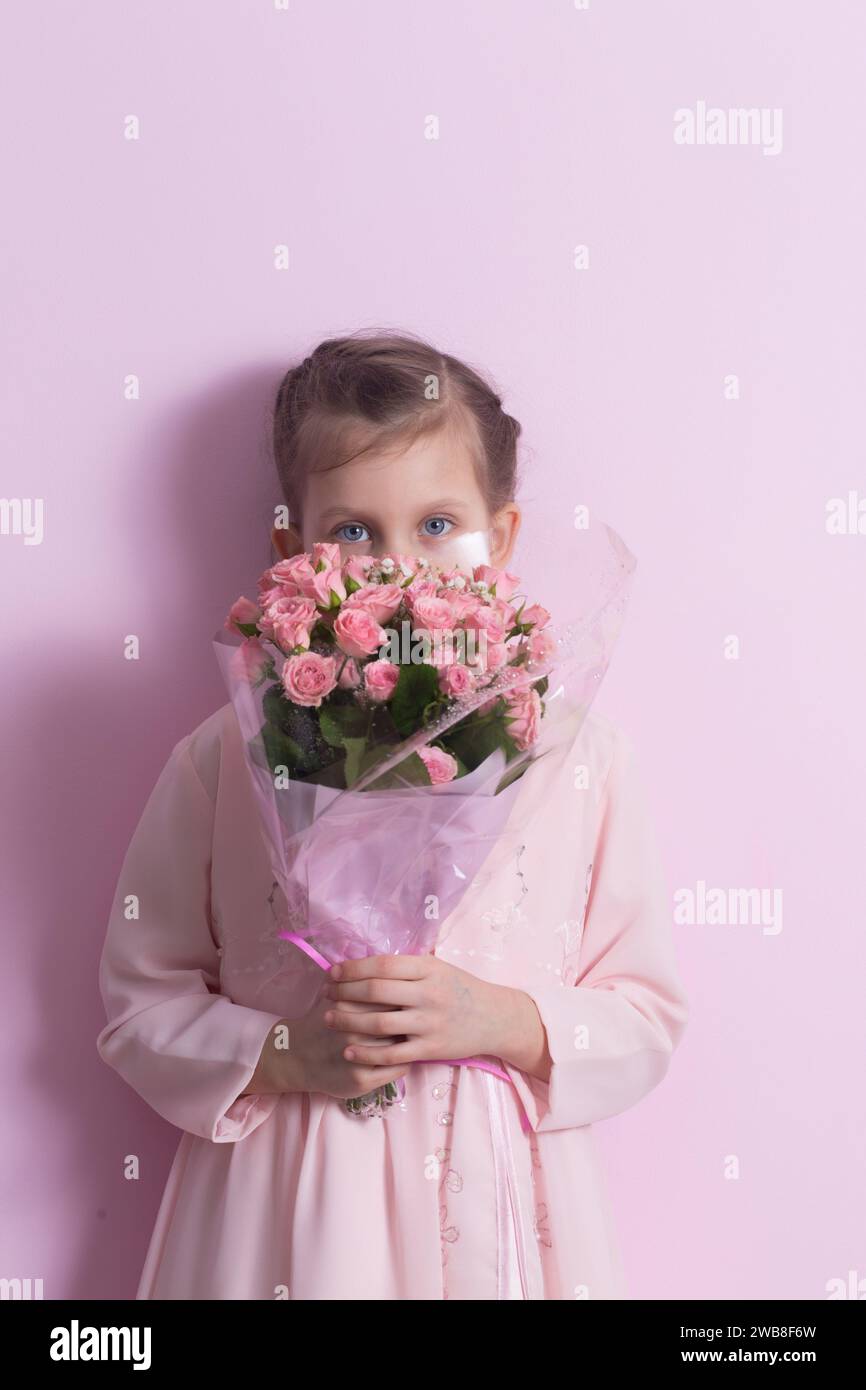 A cute little girl in a pink dress holds a bouquet of pink roses on a ...