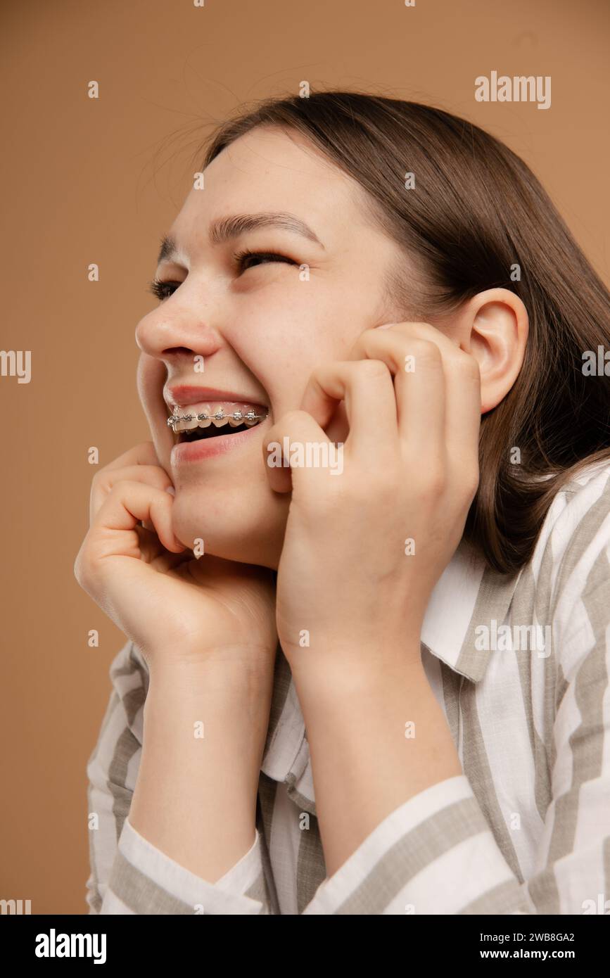 happy woman with braces with open smile look away on beige background Stock Photo