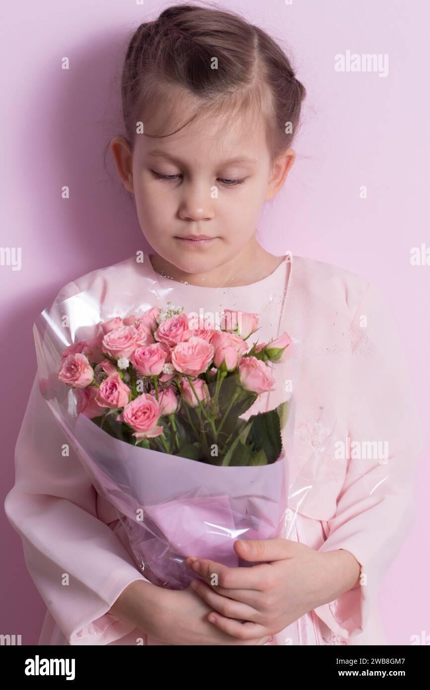 A cute little girl in a pink dress holds a bouquet of pink roses on a ...